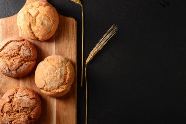 Lezzetli çörekleri ve siyah arka planda buğday kulakları olan bir tahta.