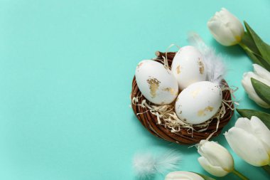 Paskalya yumurtalı yuva, turkuaz arka planda tüyler ve laleler