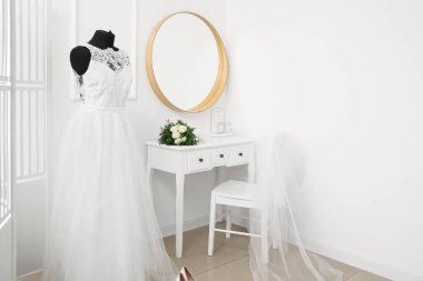 Gelinlikli manken ve aydınlık odadaki beyaz tuvalet masasında düğün buketi.