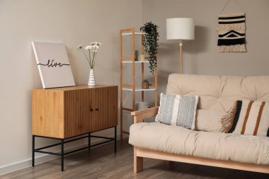 Çekmeceleri, resimleri ve çiçekleri oturma odasında olan şık bej bir kanepe.