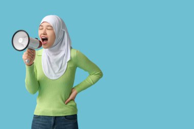 Genç Asyalı Müslüman kadın mavi arka planda megafona bağırıyor. Ulusal Duyulma Günü
