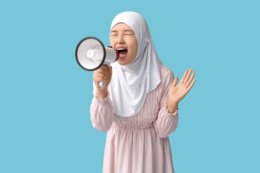 Genç Asyalı Müslüman kadın mavi arka planda megafona bağırıyor. Ulusal Duyulma Günü