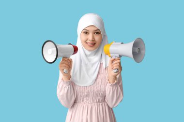 Mavi arka planda megafonları olan genç Asyalı Müslüman kadın. Ulusal Duyulma Günü