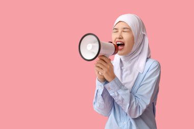 Genç Asyalı Müslüman kadın pembe arka planda megafona bağırıyor. Ulusal Duyulma Günü