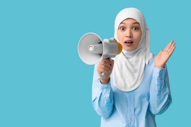 Asyalı genç Müslüman kadını mavi arka planda megafonla şoke etti. Ulusal Duyulma Günü