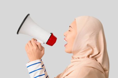 Genç Asyalı Müslüman kadın gri arka planda megafona bağırıyor. Ulusal Duyulma Günü