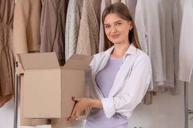 Soyunma odasında giysi kutusu ve giysileri olan güzel, genç ve mutlu bir kadın.