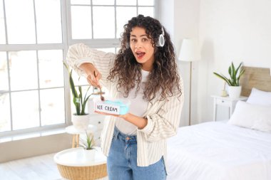 Kulaklıklı Afro-Amerikalı genç bir kadın yatak odasında bir sepet dondurmayla şok oldu.