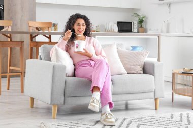 Evdeki kanepede oturan bir sepet dondurmalı güzel Afro-Amerikalı kadın.