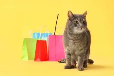 Sarı arka planda sevimli kedi ve alışveriş torbaları.