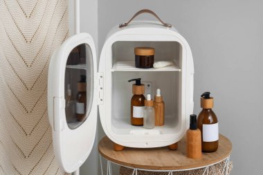 Gri duvarın yanında küçük buzdolabı ve kozmetik ürünleri olan bir masa.