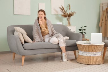 Evde tıbbi sprey kullanan boğaz ve battaniyeli hasta genç bir kadın.