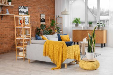 Gri kanepeleri, puf ve çiçekleri olan modern oturma odasının içinde.