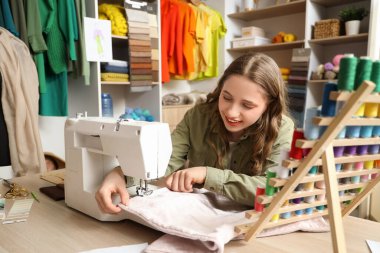 Atölyedeki masada makineyle dikiş diken kadın terzi.