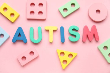 Kelime AUTISM ve pembe arka planda eğitici oyuncaklar. Üst görünüm
