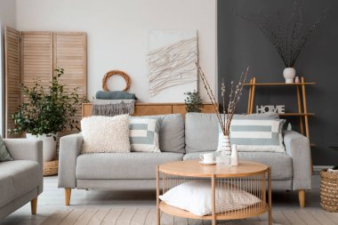 Kanepesi ve vazolarında söğüt dalları olan modern oturma odasının içinde.