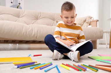 Evde keçeli kalemleri ve defteriyle resim çizen sevimli bir çocuk.