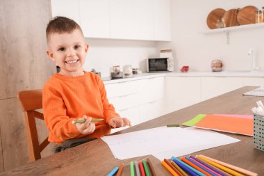 Mutfaktaki masasında keçeli kalemlerle çizen sevimli küçük çocuk.