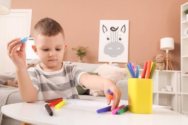 Evdeki masada keçeli kalemlerle resim çizen sevimli küçük çocuk.