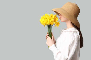 Gri arka planda narsisli çiçeklerle dolu buketi olan güzel genç bir kadın.