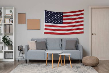 Beyaz duvarda kanepe, sehpa ve Amerikan bayrağı olan bir oda.