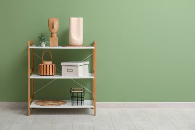 Yeşil duvarın yanında dekoru ve dekoru olan modern raf ünitesi.