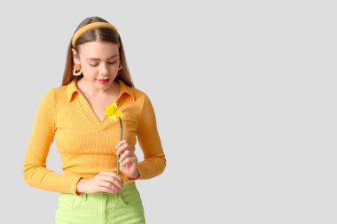 Gri arka planda nergis çiçeği olan güzel genç bir kadın.