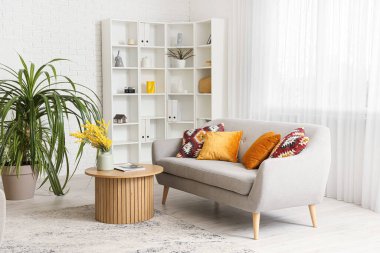 Konforlu kanepe, çiçekli kahve masası ve oturma odasında çiçek.