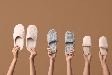 Bej arka planda farklı terlikler tutan kadın eller.