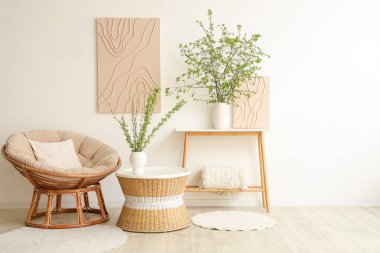 Rahat koltuk, kahve masası ve aydınlık oturma odasında çiçek açan dalları olan vazolar.