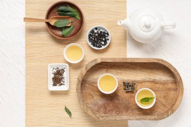 Fincanlı çaydanlık, bir kase kuru çay ve beyaz arka planda yapraklar.