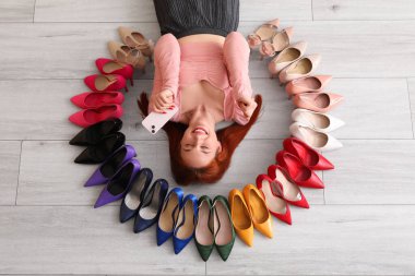 Genç bir kadın ve beyaz ahşap arka planda farklı yüksek topuklu ayakkabılar.