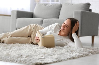 Genç ve güzel bir kadın kitap okuyor ve evde yerde dinleniyor.