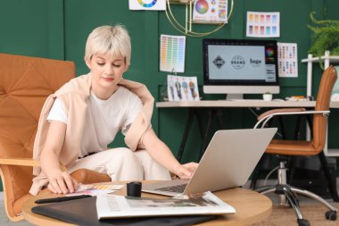 Young female graphic designer working with laptop on table in office