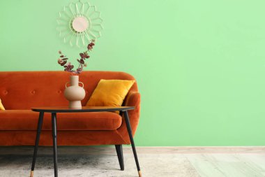 Oturma odasındaki kanepenin yanındaki masada yapay okaliptüs dalları olan vazo.