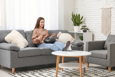 Oturma odasında siyah kanepede glukofon çalan genç bir kadın.