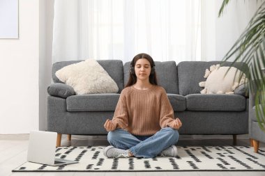 Genç bir kadın oturma odasında yerde meditasyon yapıyor.