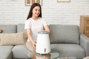 Genç kadın rahat koltukta oturuyor ve modern nemlendiriciyi açıyor şık oturma odasında.