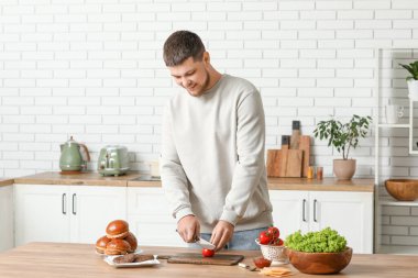 Genç adam mutfakta domates doğruyor.