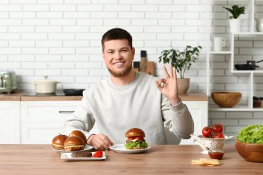 Lezzetli burgerleri olan genç adam mutfakta iyi görünüyor.