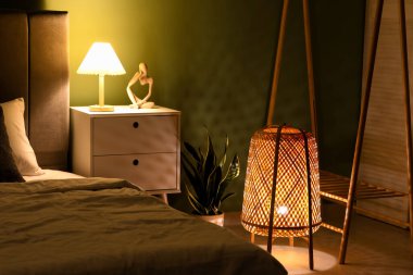 Yatak odasının içinde gece lamba, yatak ve komodin var.