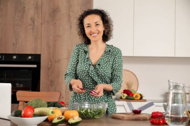 Mutfakta soğan doğrayan olgun bir kadın sebze salatası pişiriyor.