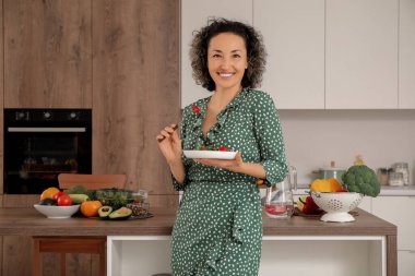 Mutfakta sebze salatası yiyen olgun bir kadın.