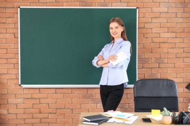 Sınıfta temiz yazı tahtasının yanında bez parçası olan kadın öğretmen.