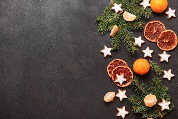 Yıldız şeklinde mandalinli zencefilli kurabiye, kurutulmuş portakal ve siyah arkaplanda köknar dalları