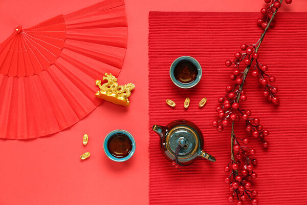 Чайник с чашками чая, статуэткой золотого дракона, веером и веткой вибурнума на красном фоне