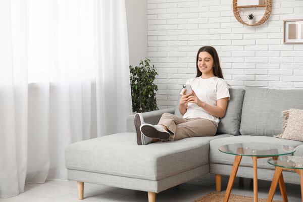 Молодая женщина болтает с мобильным телефоном на сером диване в гостиной