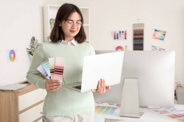 Ofisinde dizüstü bilgisayarı ve renk paletleri olan güzel bir iç mimar.