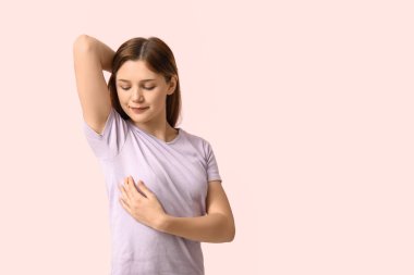 Açık pembe arka planda göğüslerini kontrol eden genç bir kadın.