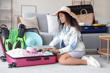 Genç Afro-Amerikalı kadın otel odasında seyahat aksesuarlarıyla bavulunu boşaltıyor.